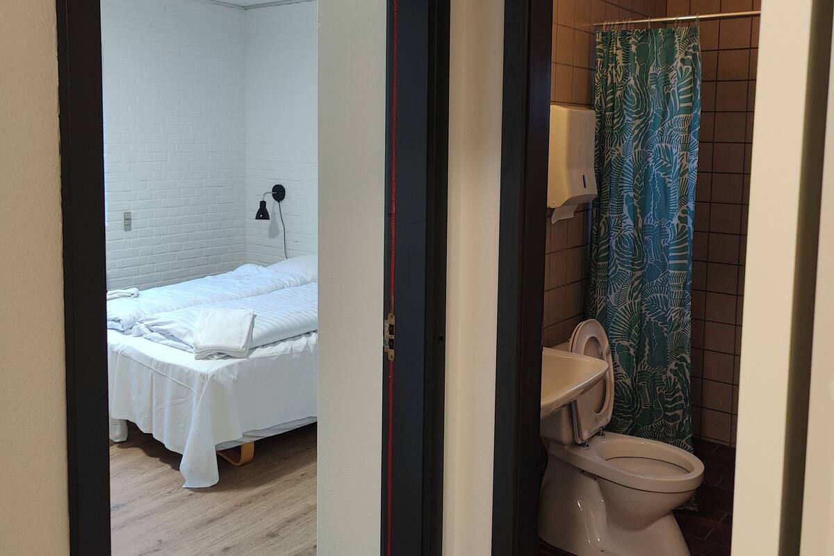 A hotel room with a bed, a bathroom with a toilet and shower curtain, and a hallway.