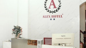 Un mostrador de recepción con el logotipo del Hotel Alex, un pequeño adorno navideño y un cartel que indica la disponibilidad de WiFi.