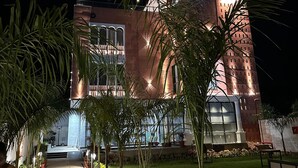 A modern building with a central tower, a pathway lined with potted plants, and a well-lit entrance. - THE LOVE PASSION KARMA CLUB & RESORT (Udaipur)