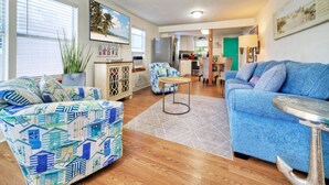 Ein geräumiges Wohnzimmer mit blauem Sofa, einem gemusterten Sessel und einem Essbereich im Hintergrund.
