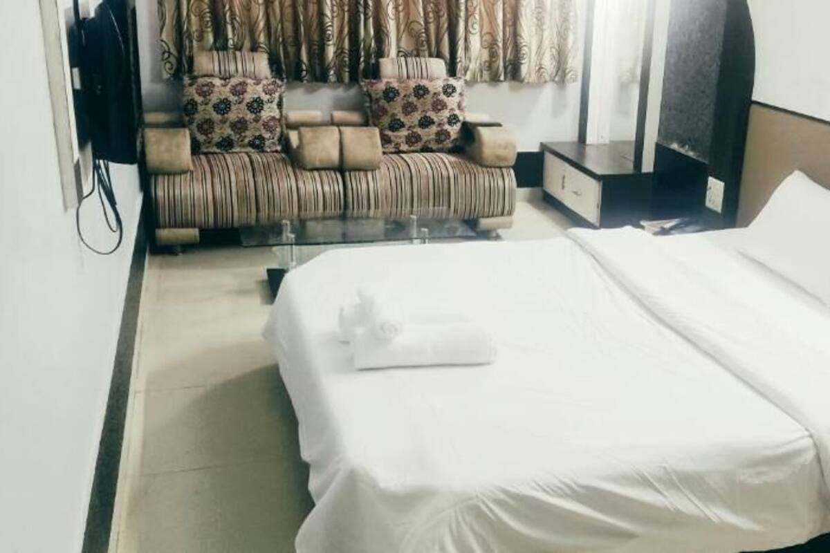 A hotel room with a bed, a sofa, a nightstand, and a TV.