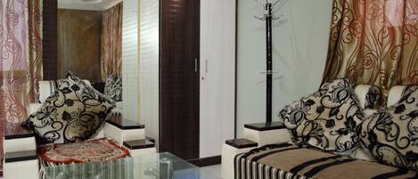 A living room with a sofa, a glass coffee table, a side table, a coat rack, and a door.