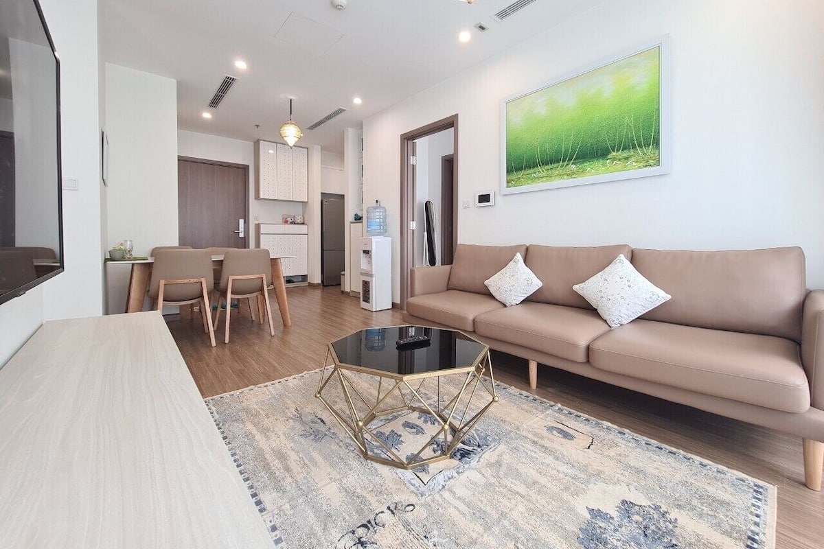 Uma sala de estar moderna com um sofá bege, uma mesa de centro de vidro e um espaço de jantar com uma mesa e cadeiras de madeira.
