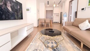 A modern living room with a flat-screen TV, a glass coffee table, a beige sofa, and a dining area with a table and chairs. - Vinhome Skylake Luxury Apartment  (Hanoi)