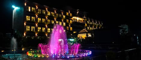 A hotel with a water fountain display at night.