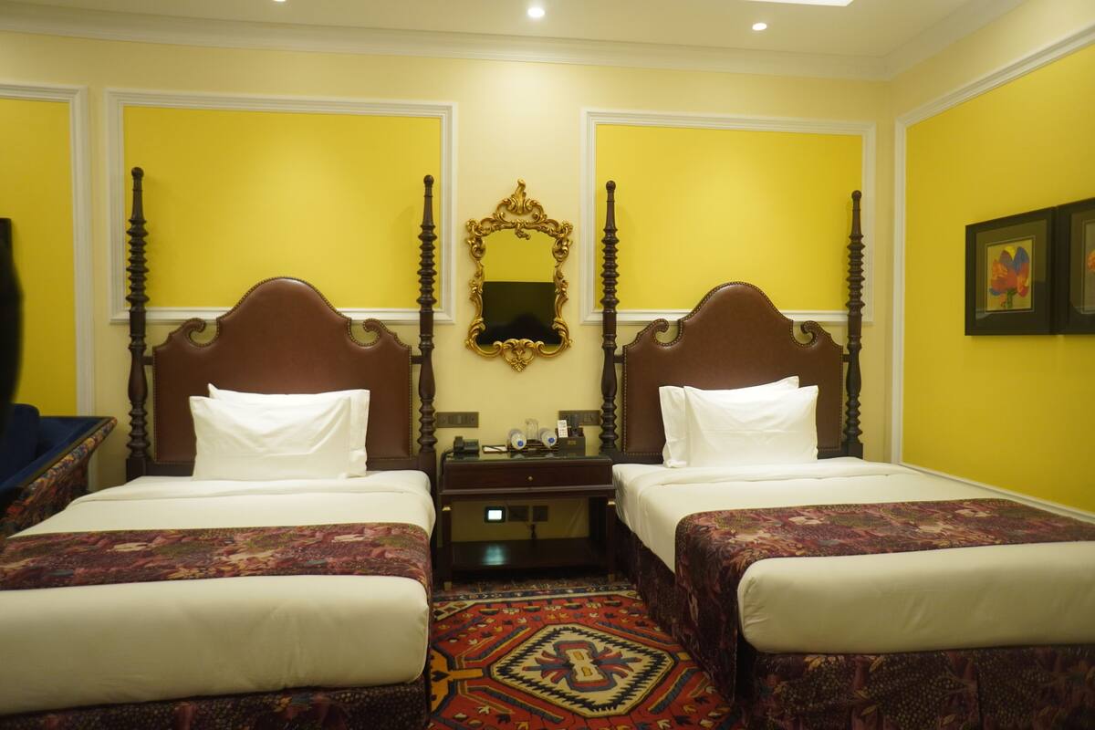 A hotel room with two beds, a large mirror, and a small table with a clock.