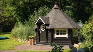 A log cabin with a conical roof, surrounded by lush greenery and a paved path. - Group House in Twente with Hot Tub (Losser)