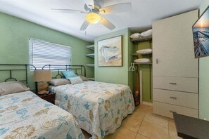 Un dormitorio con dos camas, un ventilador de techo, una ventana con persianas, un cuadro y un armario.