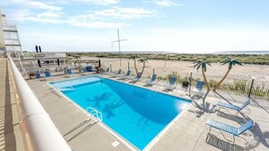 Una piscina amb gandules i palmeres, amb vista a una platja.