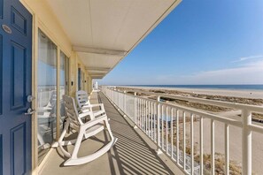 Un balcon avec des fauteuils à bascule blancs, une balustrade blanche et une vue sur la plage.