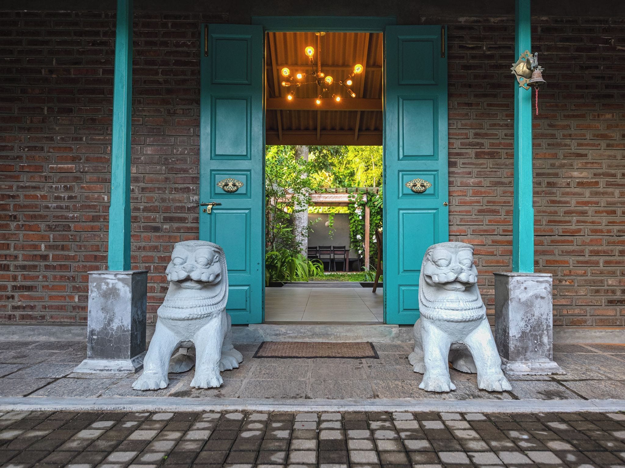 A building entrance with two stone lion statues, a teal door, and a brick wall.