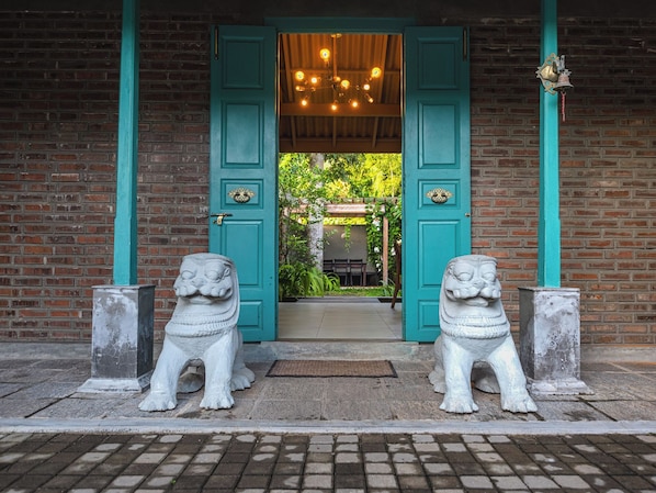 A building entrance with two stone lion statues, a teal door, and a brick wall. - The Chariot Hikkaduwa (Hikkaduwa)