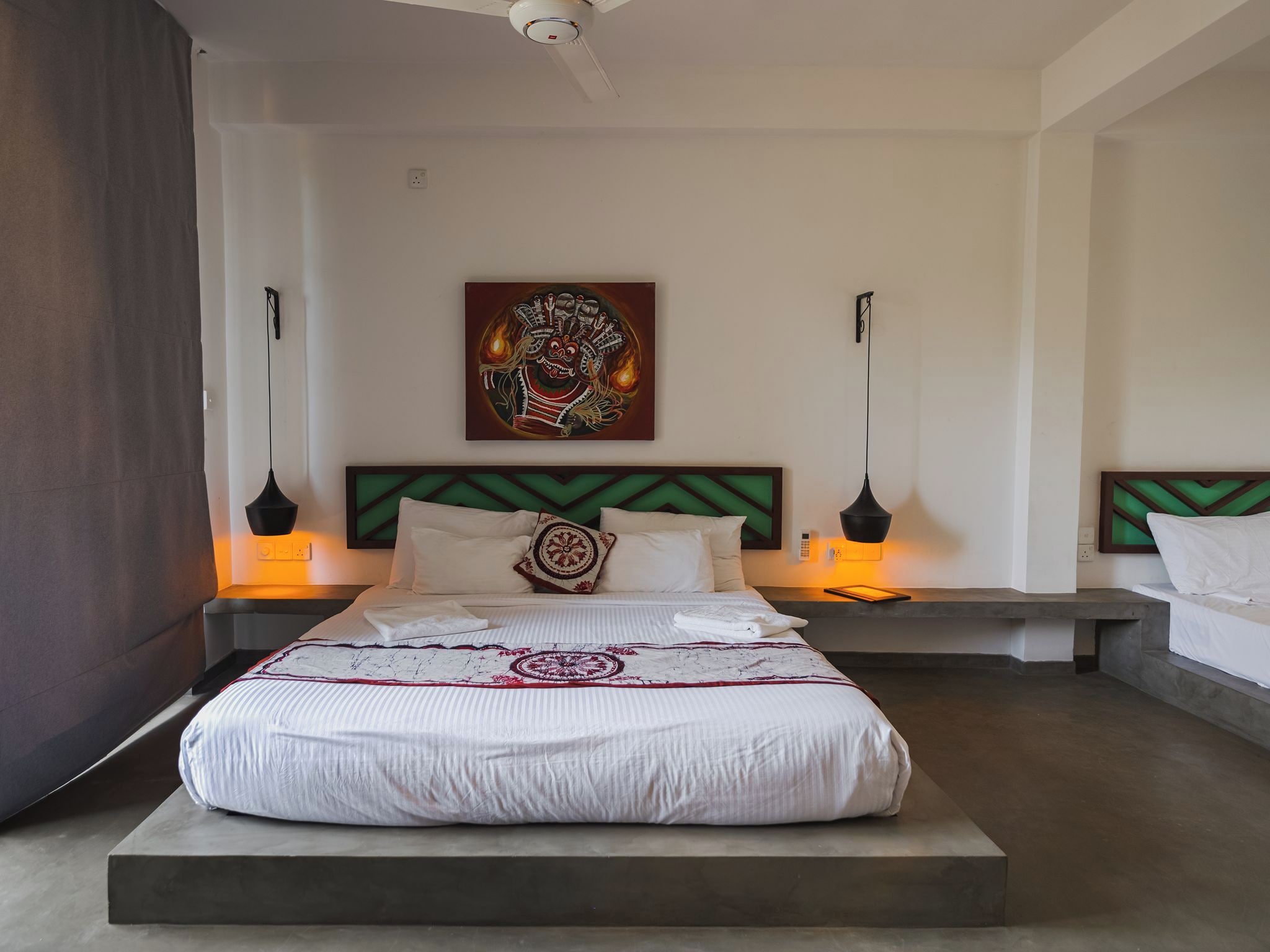 A hotel room with a large bed, a headboard with a geometric pattern, a wall-mounted artwork, bedside lamps, and a ceiling fan.
