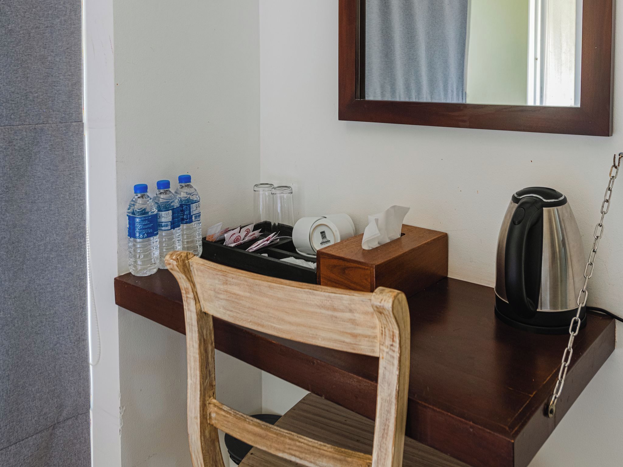 A wooden desk with a chair, a water bottle, a tissue box, a glass jar, and a kettle.