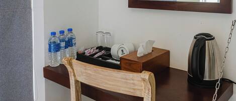 A wooden desk with a chair, a water bottle, a tissue box, a glass jar, and a kettle.