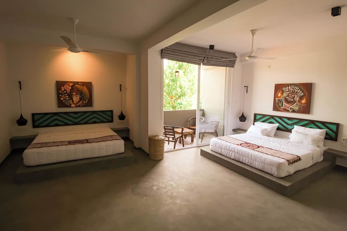 Een hotelkamer met twee bedden, plafondventilatoren, kunstwerken en uitzicht op de omgeving.