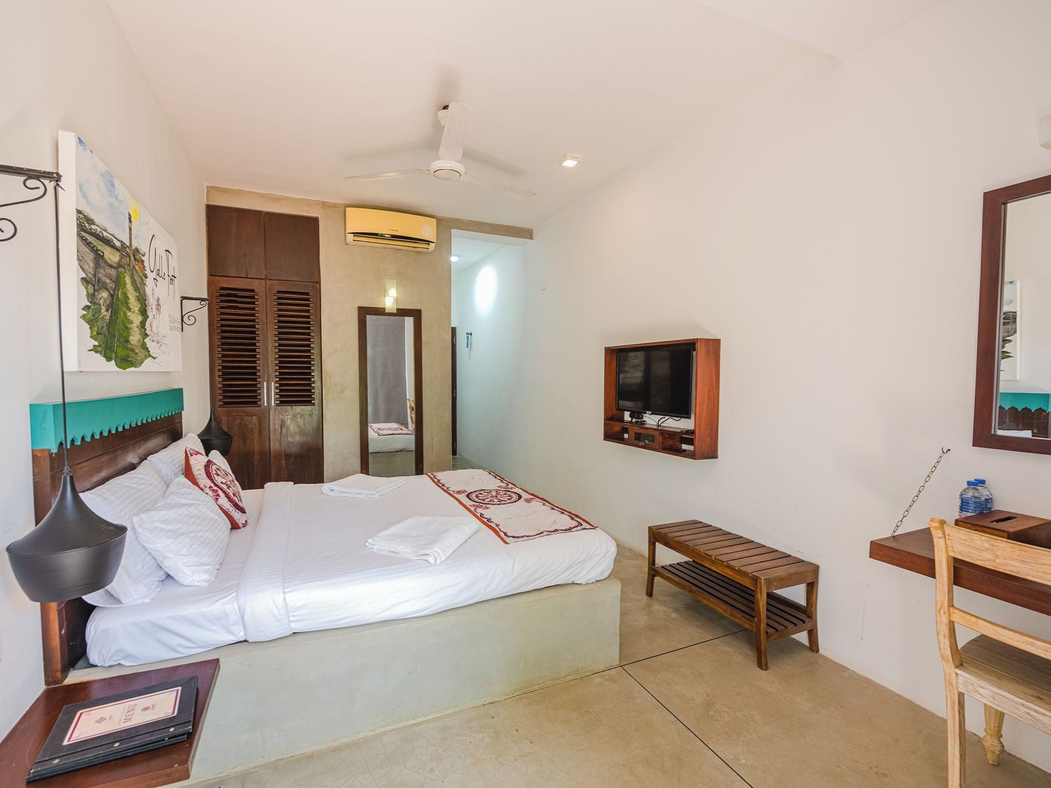 Habitación de hotel con cama, escritorio, silla, televisor y ventilador de techo.