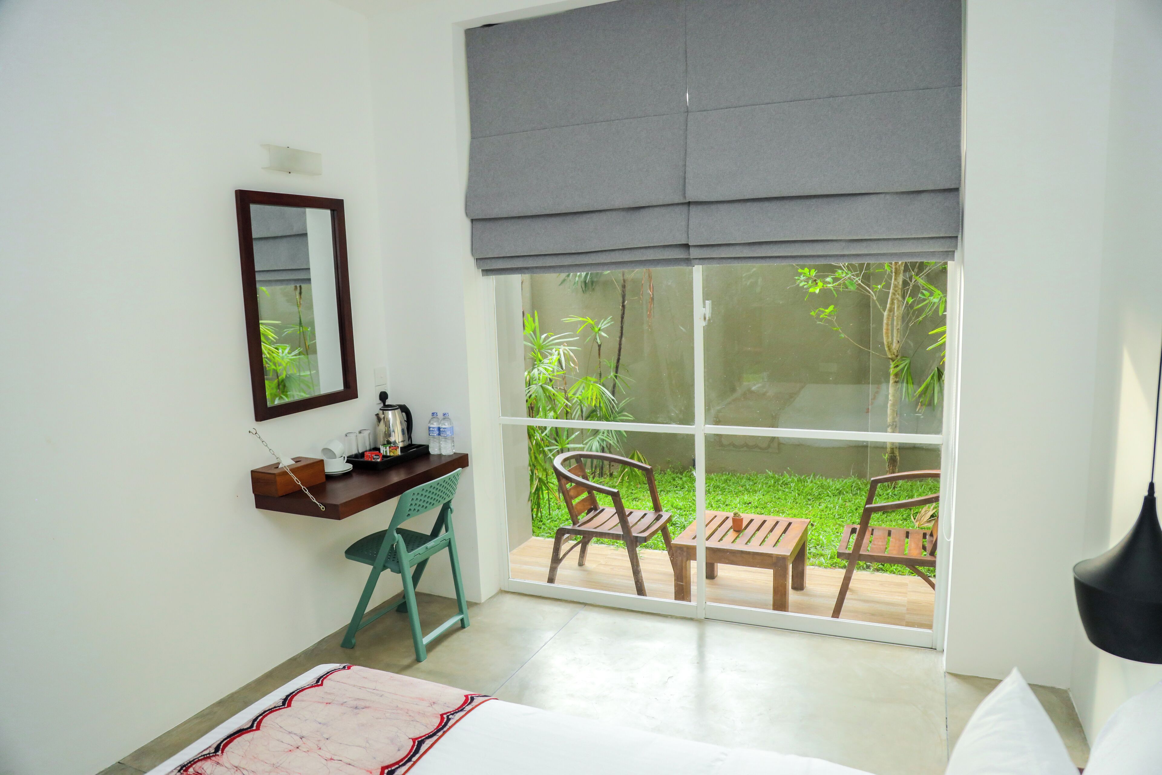 Habitación de hotel con escritorio, silla y vistas a un jardín a través de un amplio ventanal.