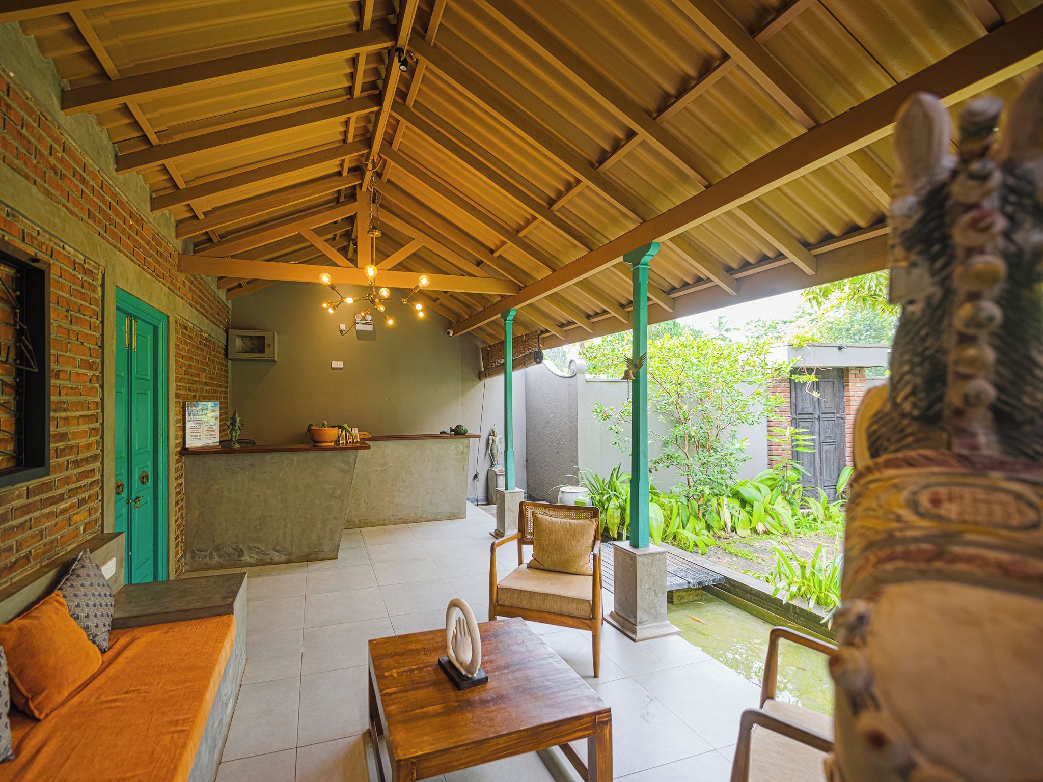 A covered outdoor seating area with a brick wall, a reception desk, and a view of a garden.