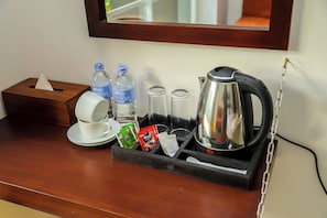 Cantinho de café em quarto de hotel, com cafeteira, chávenas, caixa de lenços de papel e garrafas de água.