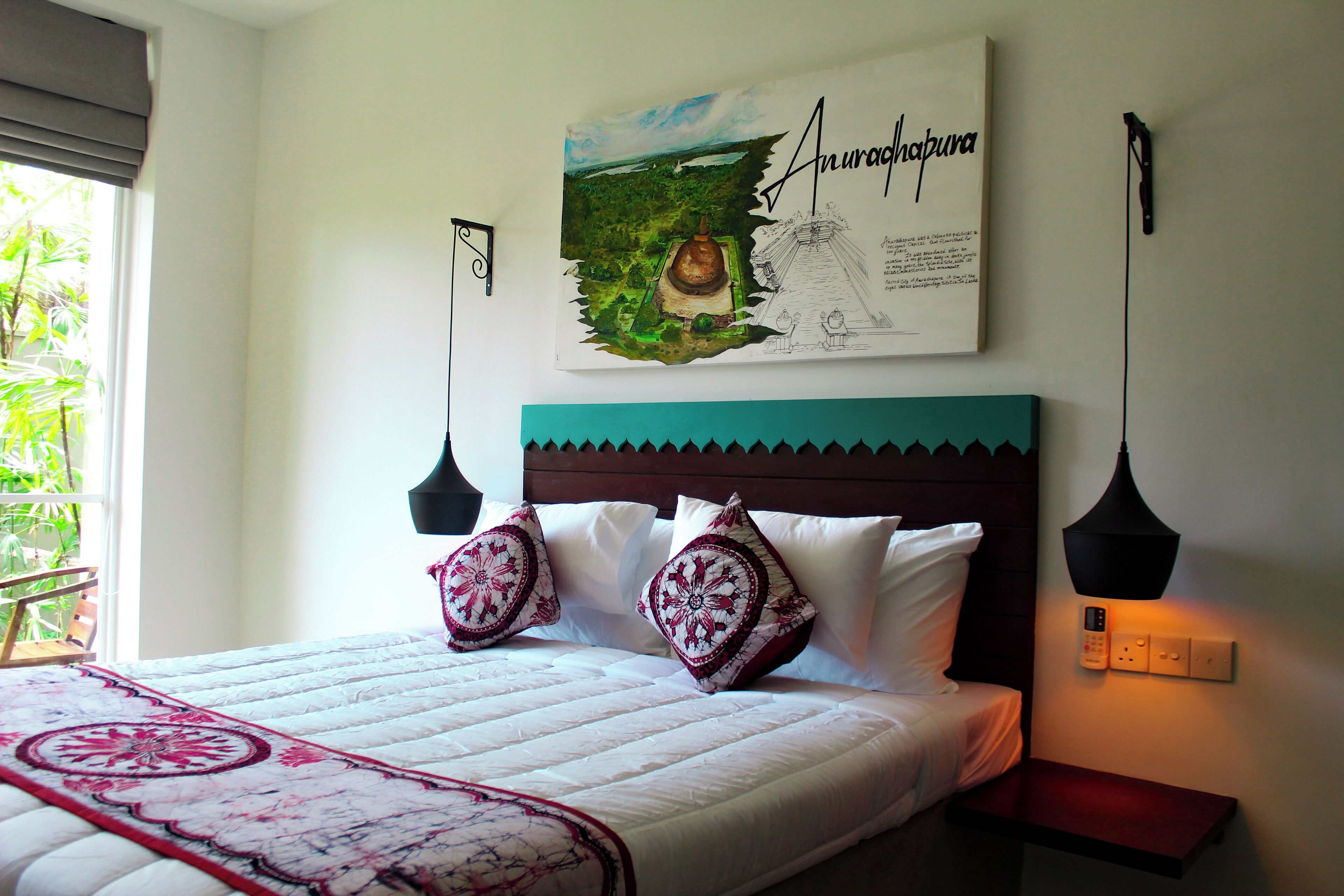 A neatly made bed with a floral bedspread, a headboard with a teal accent, and a wall-mounted artwork depicting a landscape and a structure.