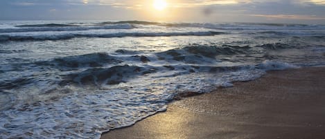 A beach with waves and a sunset.