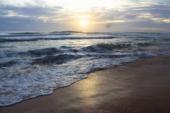 A beach with waves and a sunset.