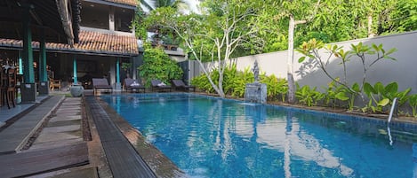 A swimming pool with a tiled deck, lounge chairs, and a statue.