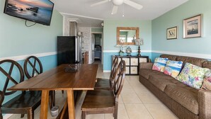 A dining area with a wooden table and chairs, a ceiling fan, a television, and a sofa with decorative pillows. - Beachside Breeze 1BR Condo with Pool & Great View! (Wildwood Crest)