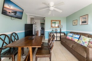 Un coin repas avec une table et des chaises en bois, un ventilateur de plafond, un téléviseur et un canapé agrémenté de coussins décoratifs.