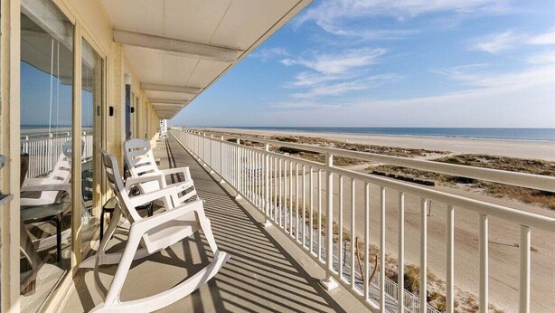 A covered balcony with white chairs, a railing, and a view of the beach. - Beachside Breeze 1BR Condo with Pool & Great View! (Wildwood Crest)