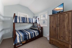 Uma cama beliche com roupa de cama listrada, um armário de madeira e uma televisão na parede.
