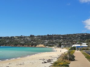 Blick auf die Küste mit einem Sandstrand, blauem Himmel und einem Hügel mit Gebäuden.