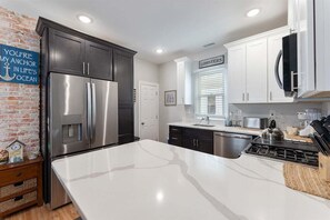 A modern kitchen with stainless steel appliances, white cabinetry, and a brick accent wall. - Spacious 4BR Home Walk to Beach, Bay, Boardwalk (Wildwood)