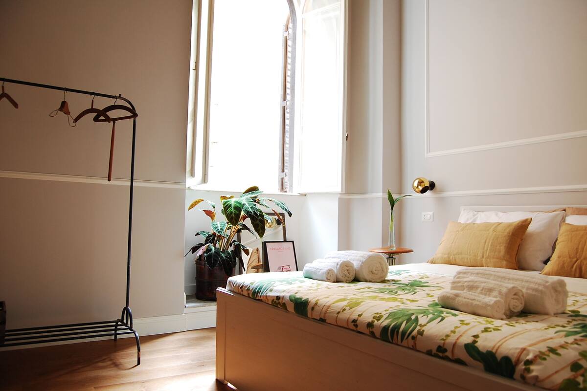 Un dormitorio con cama, ventana, planta y perchero.