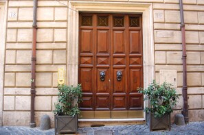 A double wooden door with a brass knocker, flanked by two potted plants. - Banco 19 b&b  (Rome)