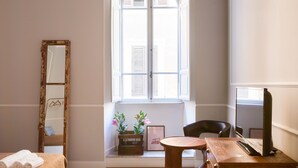 A room with a large arched window, a wooden table, a chair, a mirror, and a framed picture on a bench. - Banco 19 b&b  (Rome)