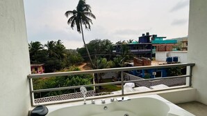 A balcony with a white bathtub, a metal railing, and a view of buildings and palm trees. - Dacha Arambol (Arambol)