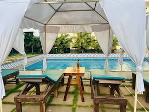 Un área de estar al aire libre techada, con una piscina al fondo.