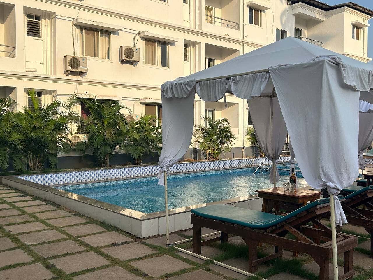 A swimming pool with a tiled edge, surrounded by lounge chairs and a covered area.