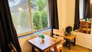 A room with a wooden table and chairs, a window with curtains, and a view of greenery outside. - Dacha Arambol (Arambol)