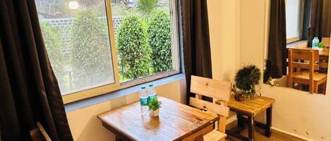 A room with a wooden table and chairs, a window with curtains, and a view of greenery outside.