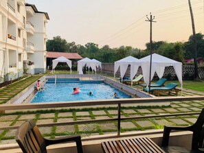 Una piscina con solárium de baldosas, rodeada de toldos blancos y sillas de descanso.