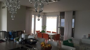 Eine moderne Küche mit einer zentralen Kochinsel, einem Essbereich mit orangefarbenen Stühlen und einem großen Fenster, das für natürliches Licht sorgt.