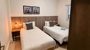 A hotel room with two beds, a wooden headboard, a nightstand with a lamp, and two framed pictures on the wall.
