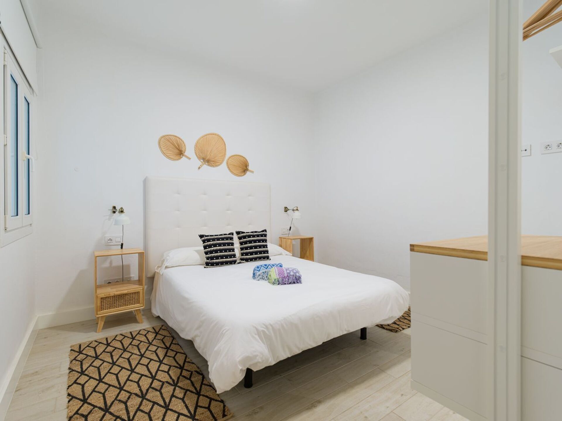 A bedroom with a bed, bedside tables, a wall-mounted lamp, a woven basket decoration, and a patterned rug.
