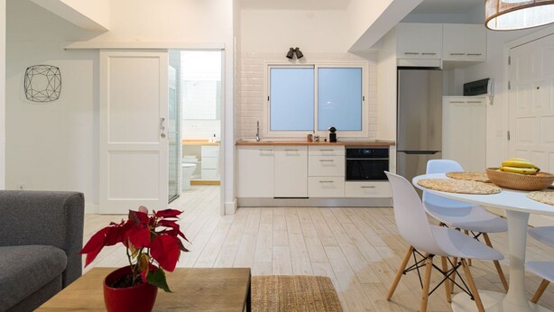 A modern kitchen with white cabinets, a dining area with white chairs, and a red potted plant on a wooden table.