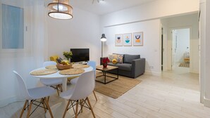 A modern living room with a dining area, a grey sofa, a flat-screen TV, and a ceiling light fixture.