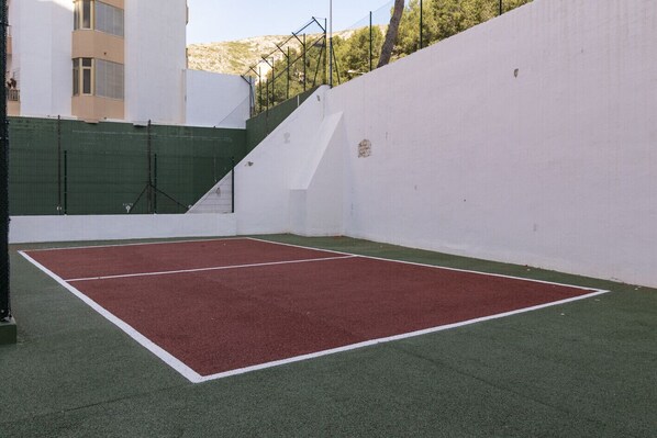 An indoor tennis court with a red playing surface and green surrounding area, enclosed by white walls and a green fence. - LAS VEGAS, ESC-1, 7º-14 (Cullera)