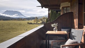 Un balcón de madera con una mesa y sillas, con vistas a un campo cubierto de hierba y montañas.